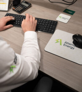 Over shoulder image of man working at a desk, with alternative energy branded mousemat and coaster